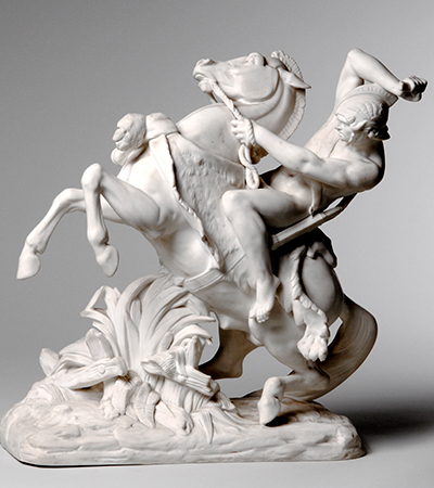White sculpture of a horse reading up with a man on its back. The man is holding onto a rope being used as a bridle and has thrown his arm up over his head. He is wearing a helmet and looks like a soldier.