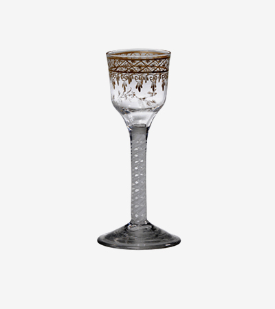 Ornate wine glass with thick stem and base and a relatively small glass for holding the wine at the top. It is decorated with brown leaves and geometric designs.