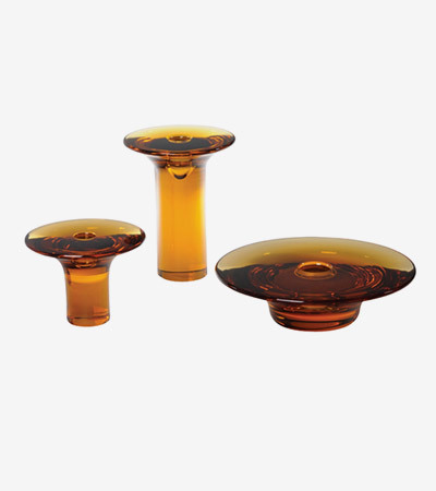 Three orange translucent candlesticks of different heights and widths. One is wide and very close to the ground, the others are taller and thinner.