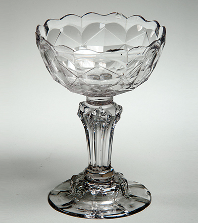 Glass dish with thick stem and base and crystal like decorations, with a wavy top.