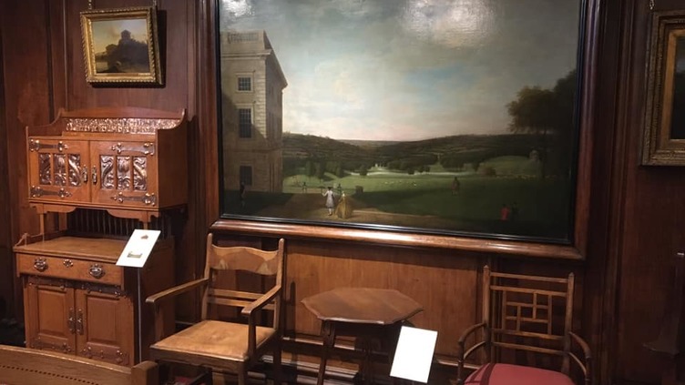 Furniture including tables, chairs and a cabinet and a large painting of a green park.