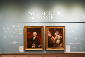 An art exhibit wall with the title "When Spencer met Stanhope." It features two portraits; one of a man in formal attire, and another of a woman and a child. Genealogical information is displayed around the portraits.