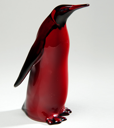 Red figure of a penguin standing upright, with its wings stretched out behind it and its head slightly tilted up.
