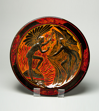 Plate with a black rim and red decorations. In the centre, a man and woman meet, he is giving her a rose.