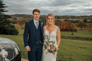 The bride and groom standing with their backs to Cannon Hall country park, smiling at the camera. Their wedding car is just to the left.