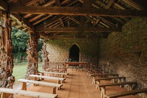 The Deer Shelter at Cannon Hall with wooden benches and chairs. The building has a vaulted roof and ornate colonnades and is made of stone