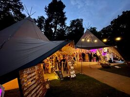 Wedding guests inside the tipi for the wedding reception, it  is lit up with different coloured lights and fairy lights.