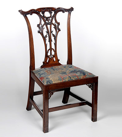 Wooden chair with soft cushion decorated with blues and reds. The back is not solid and has wooden carvings.
