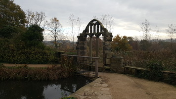 Fairyland. An ornate stone archway next to a fish pond. A path leads between the two. 