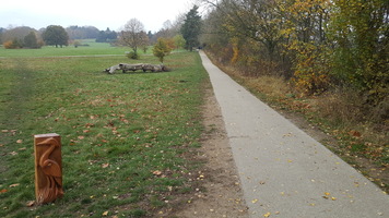 Parkland with sculpture. A path leading through the parkland with a wooden heron embossed carving on a plinth. 