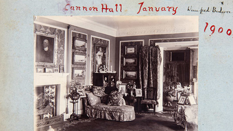 Black-and-white photo of an ornate living room with patterned wallpaper, framed paintings, a sofa, a fireplace, and various decorative objects. Handwritten text above reads “Cannon Hall January 1900.”.