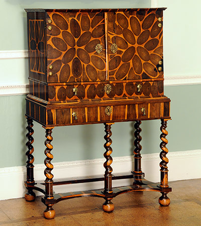 Wooden cabinet with tall legs setting it off the floor with space underneath it. It is rectangular shaped with the front being longer than it is tall, and has two doors. Orange leaf shaped decorations cover the body.