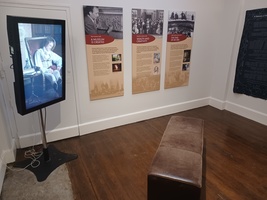 Room with a video display, three interpretation boards and a bench in the middle for seating.