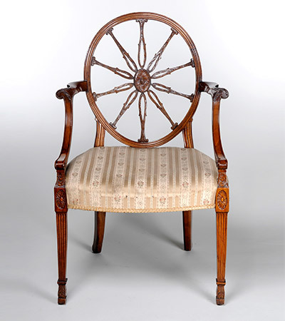 Wooden chair with a delicate white cushion. The back is in the shape of a cart wheel, circular with wooden spokes stretching into the centre.