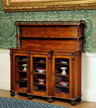 Wooden cabinet with three glass doors storing ceramic items such as plates and cake dishes.